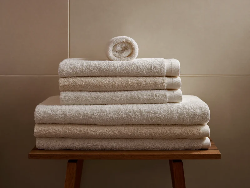 Pile de serviettes éponge épaisses et linge roulé sur un banc en bois.